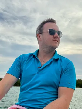 Matt Gardner in sunglasses and a blue polo, out on the water under a cloudy sky.